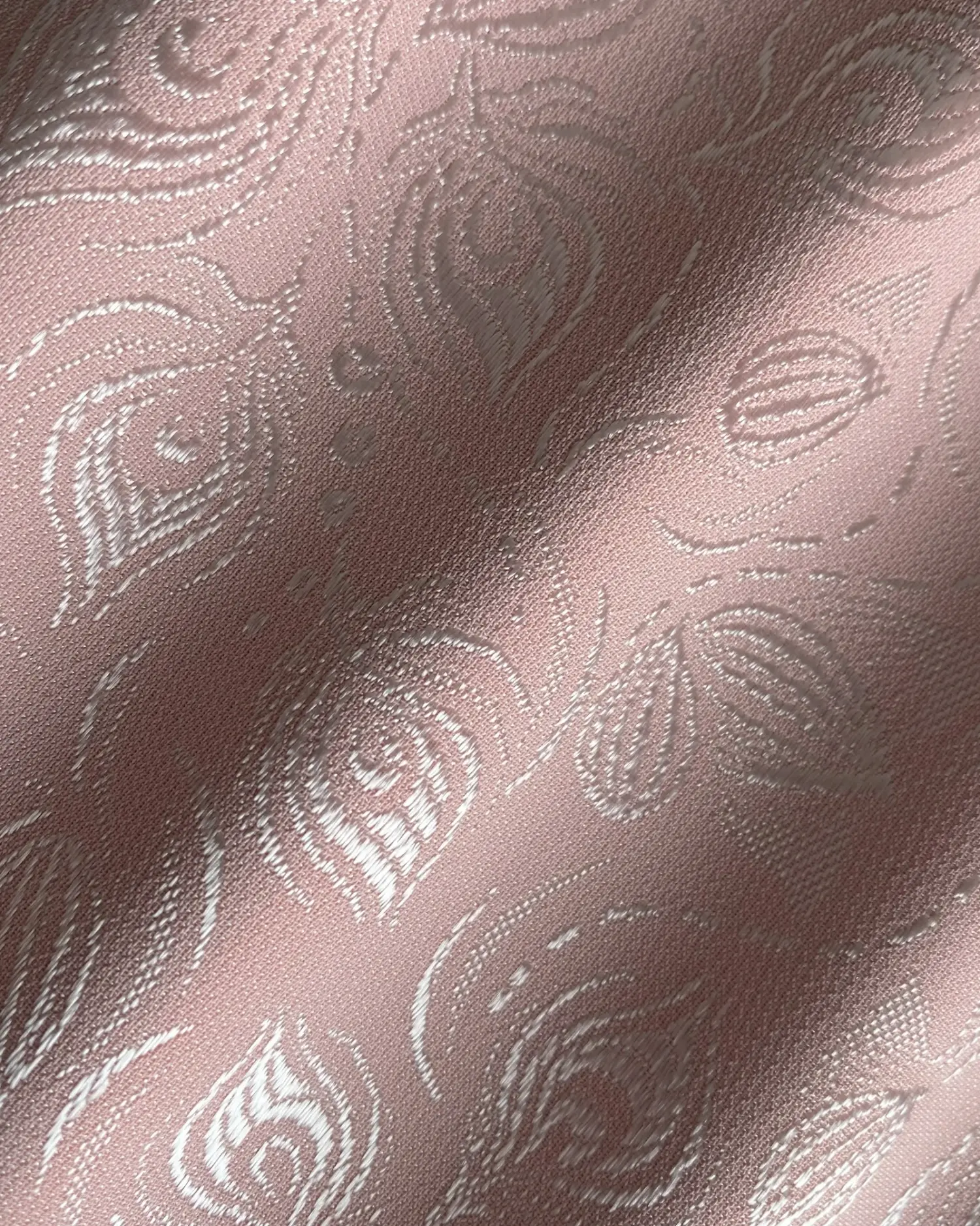 Pink fabric with intricate embossed peacock feather pattern, highlighted by soft natural light.