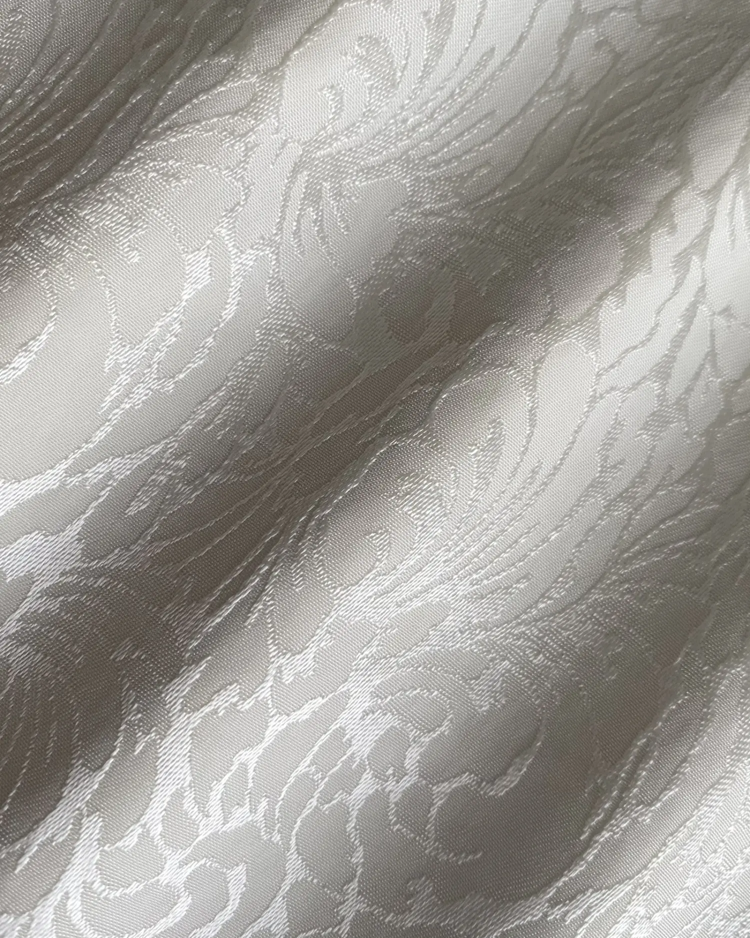 Elegant white jacquard fabric with intricate swirling pattern, capturing light and texture for a luxurious appearance.
