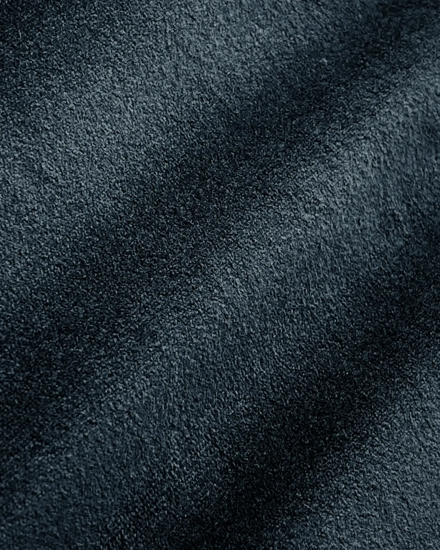 Close-up of dark textured suede fabric with subtle shading, showcasing soft surface details. Ideal for fashion or upholstery.
