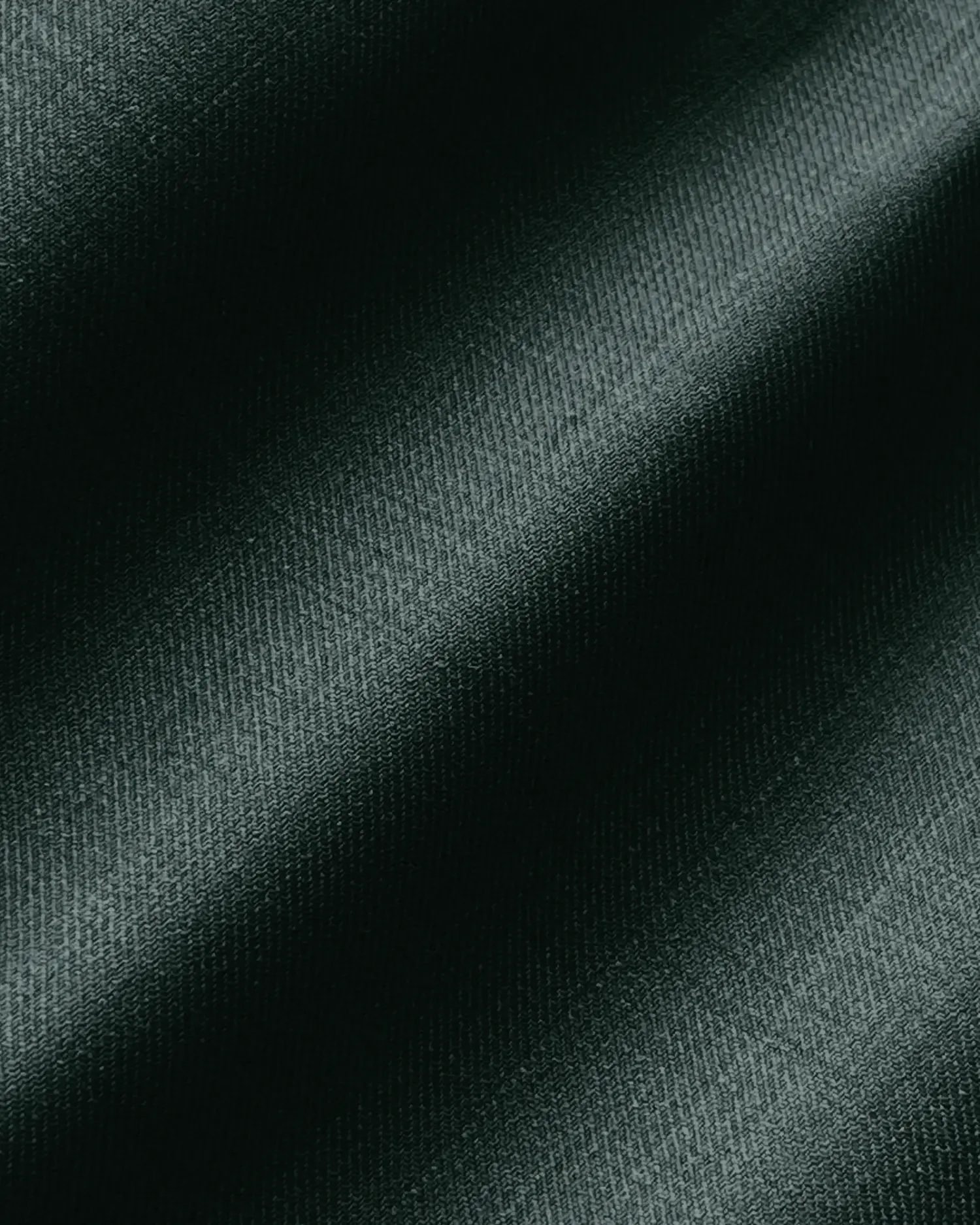 Close-up of dark green textured fabric with diagonal folds, showcasing its smooth surface and gentle sheen.