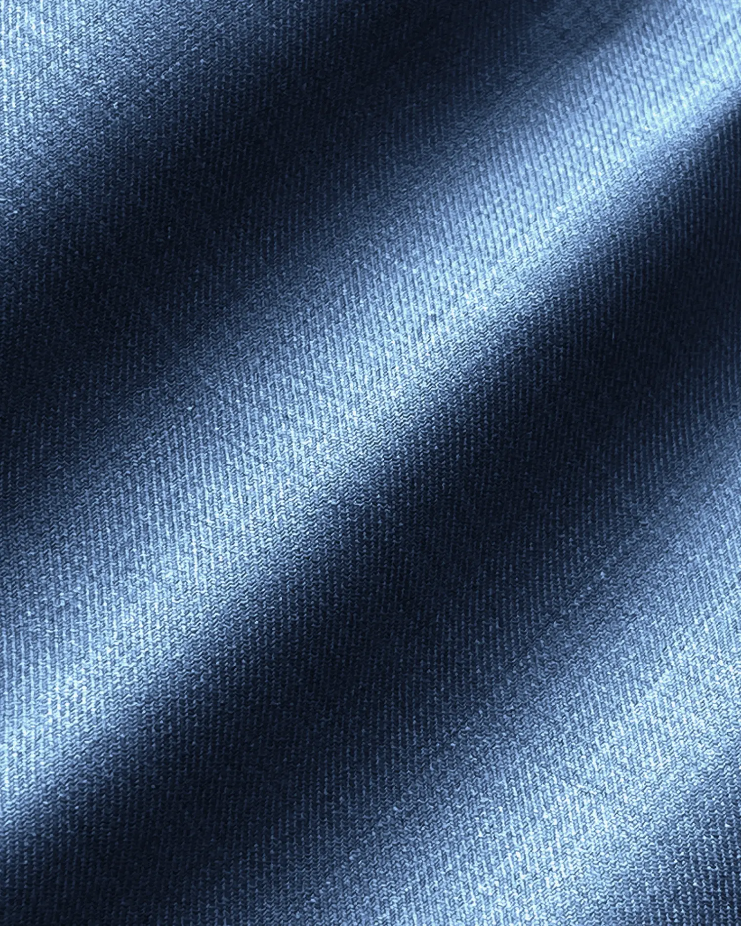 Close-up of textured blue denim fabric with diagonal shadows, highlighting woven details and rich color.