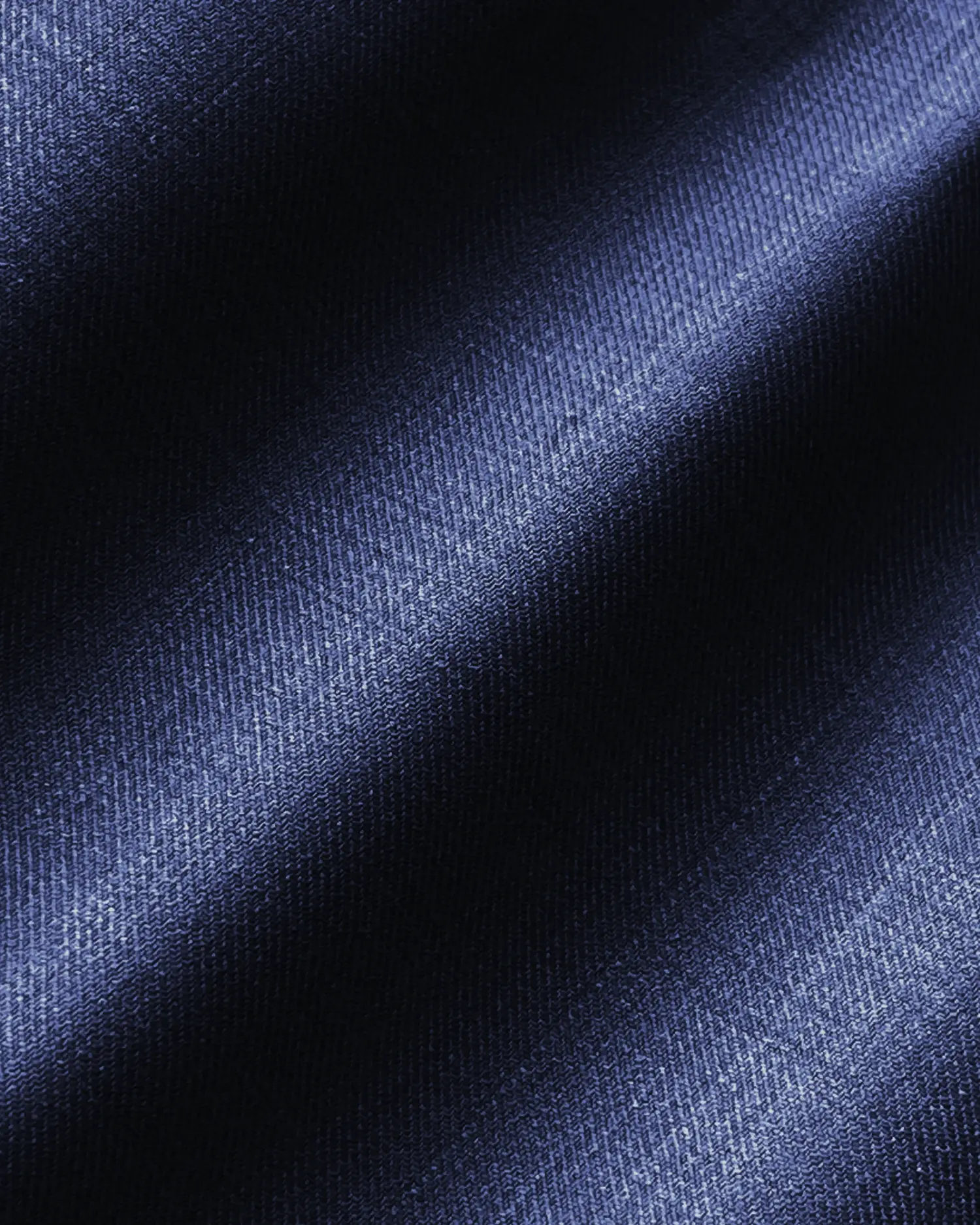 Close-up of textured blue denim fabric with diagonal shadows and a soft sheen.