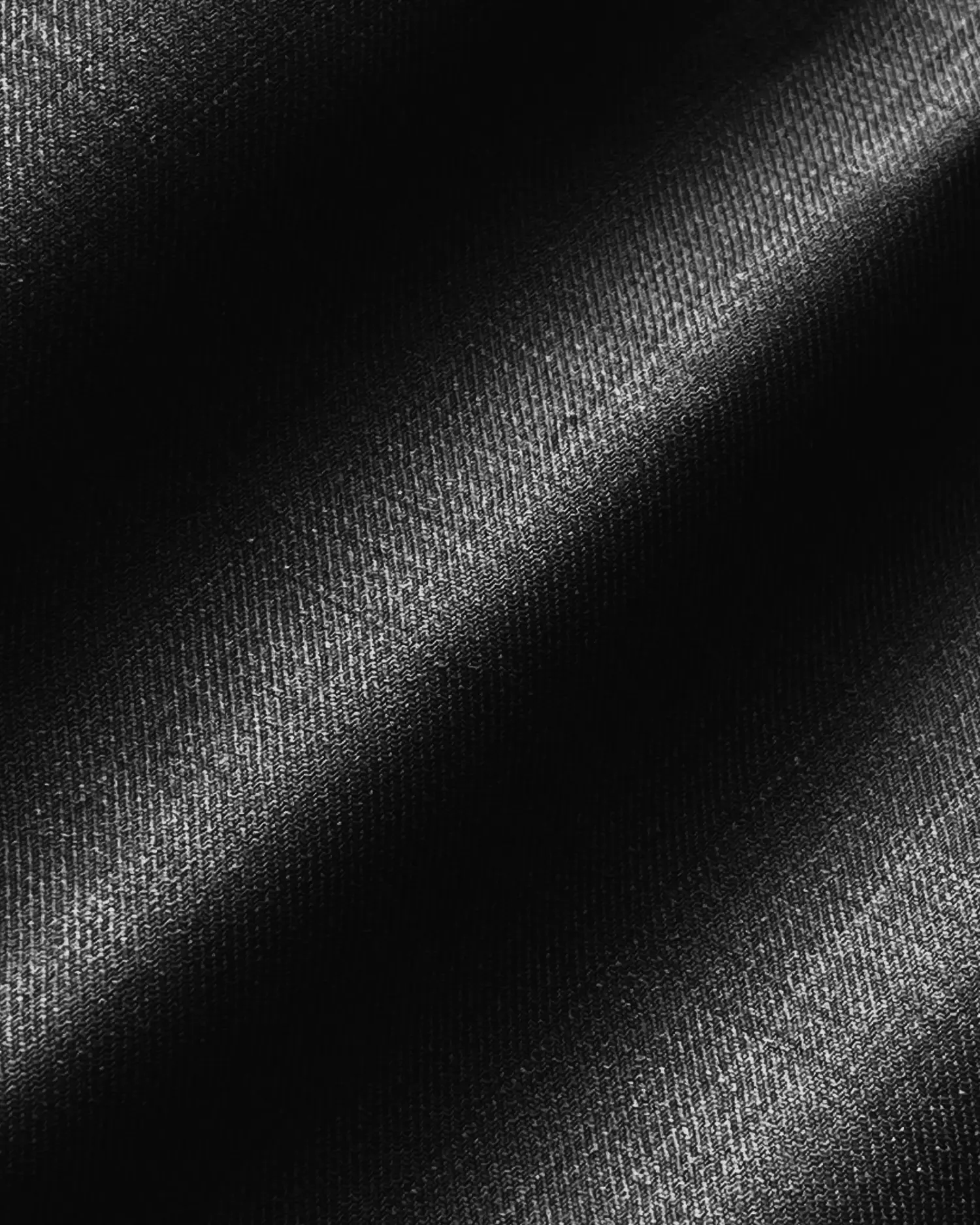Close-up of black textured fabric with light reflections, showcasing a smooth, sleek surface.