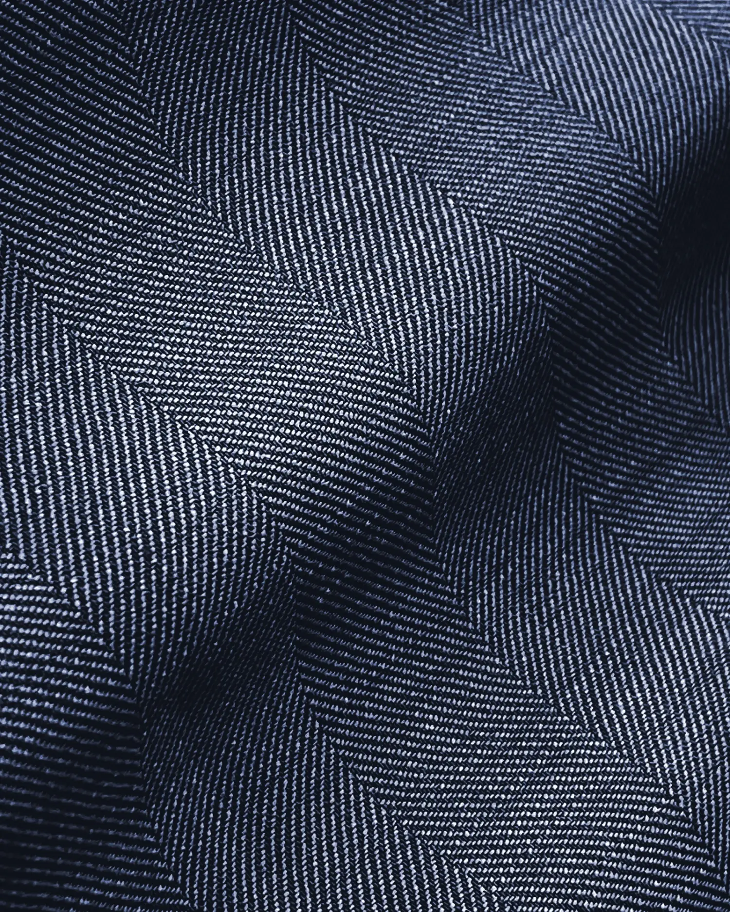 Close-up of dark blue herringbone fabric texture with subtle light and shadow contrasts.