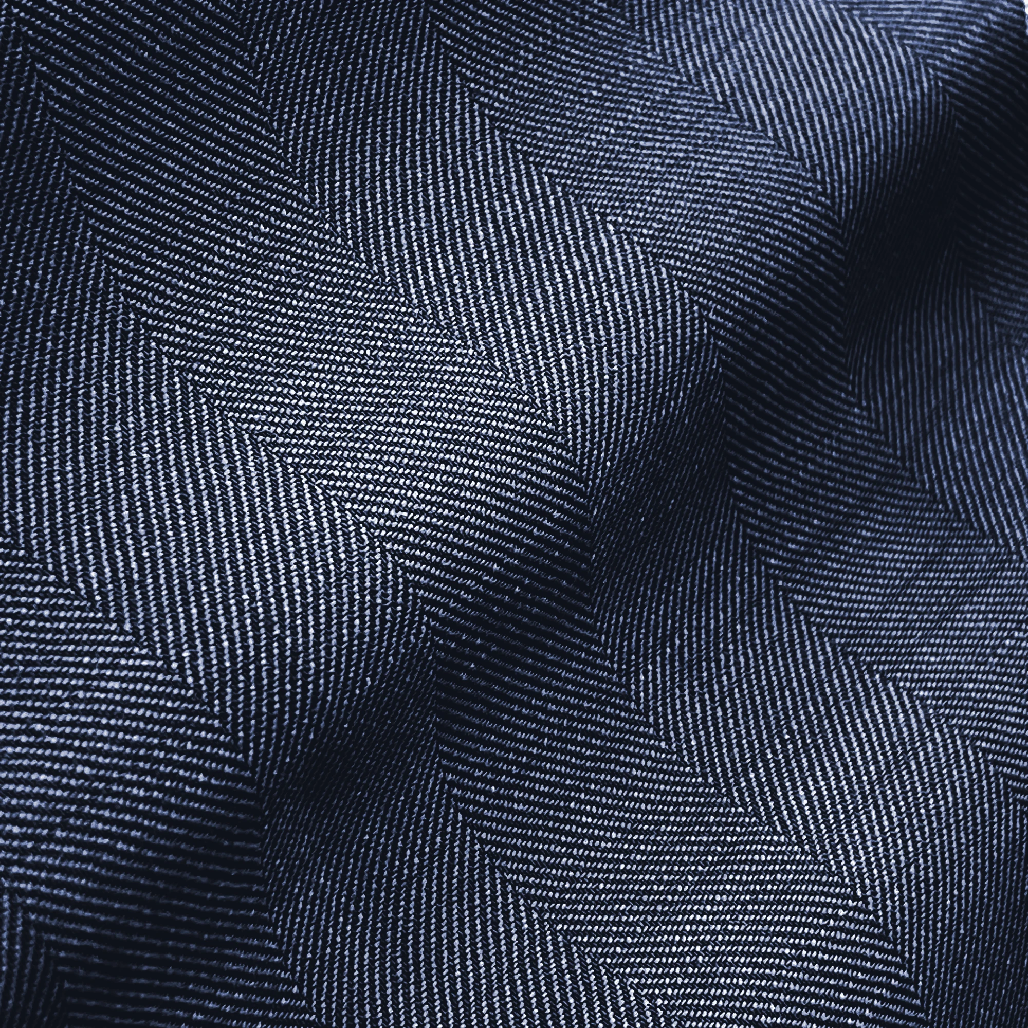 Close-up of dark blue herringbone fabric texture with subtle light and shadow contrasts.