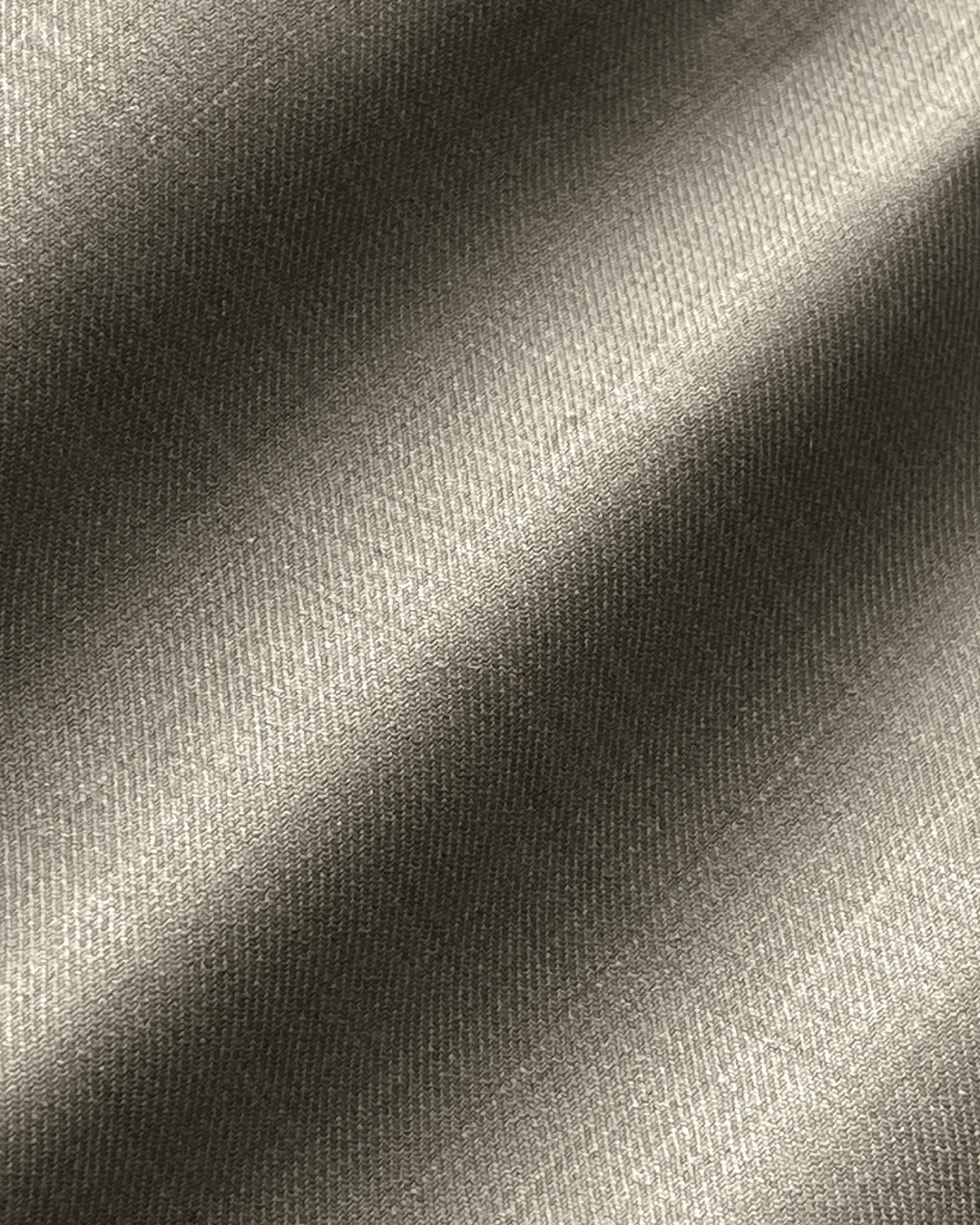 Close-up of textured fabric with diagonal weave and light shadows, showcasing a soft beige color and fine details.