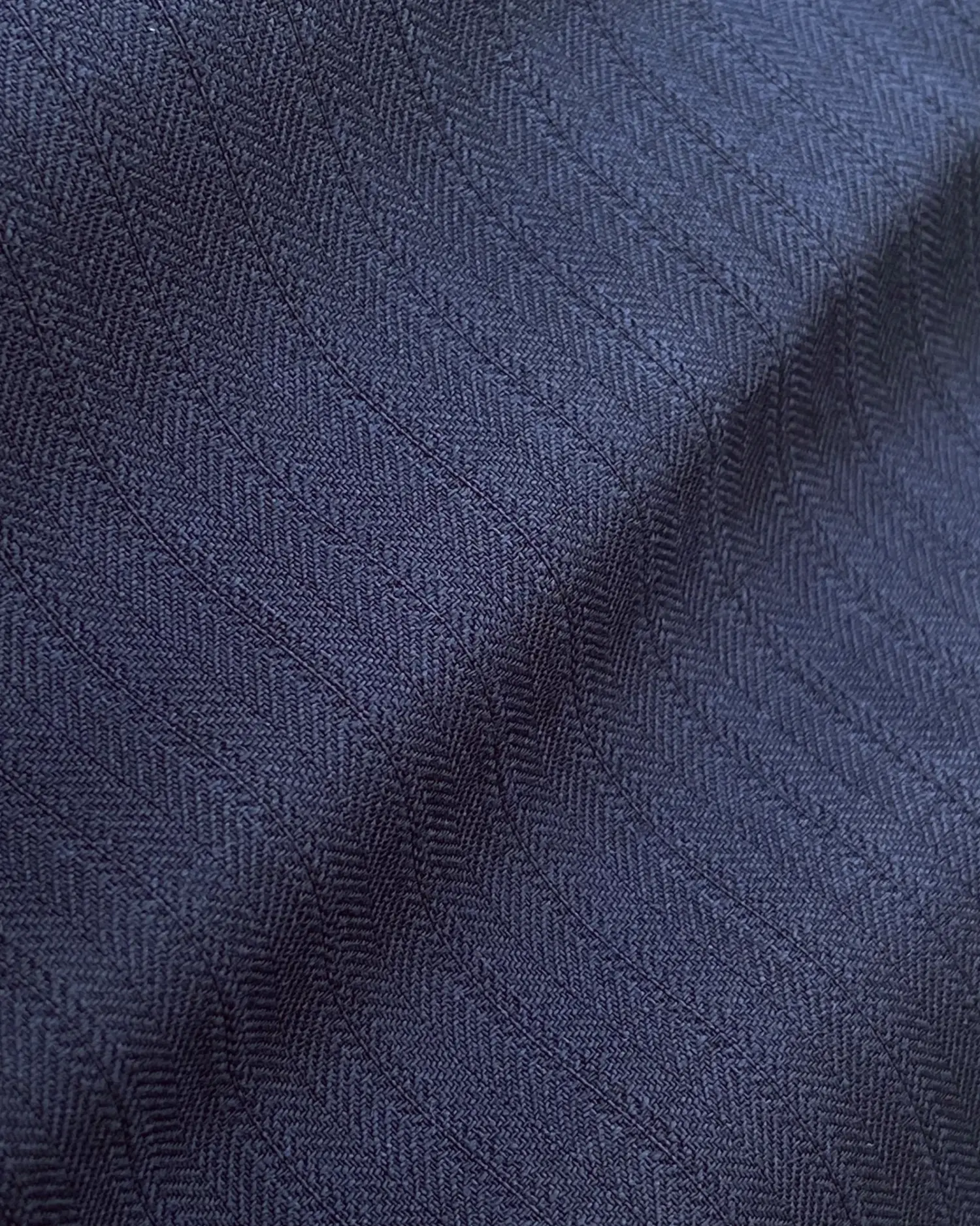 Close-up of dark blue herringbone fabric texture with a subtle chevron pattern, showcasing intricate textile details.