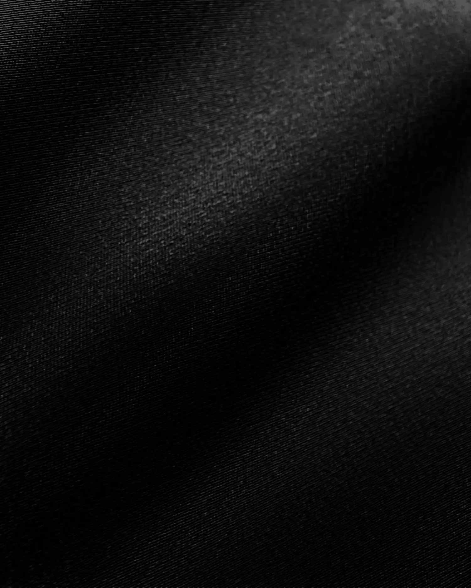 Close-up of smooth, shiny black satin fabric with subtle light reflections.