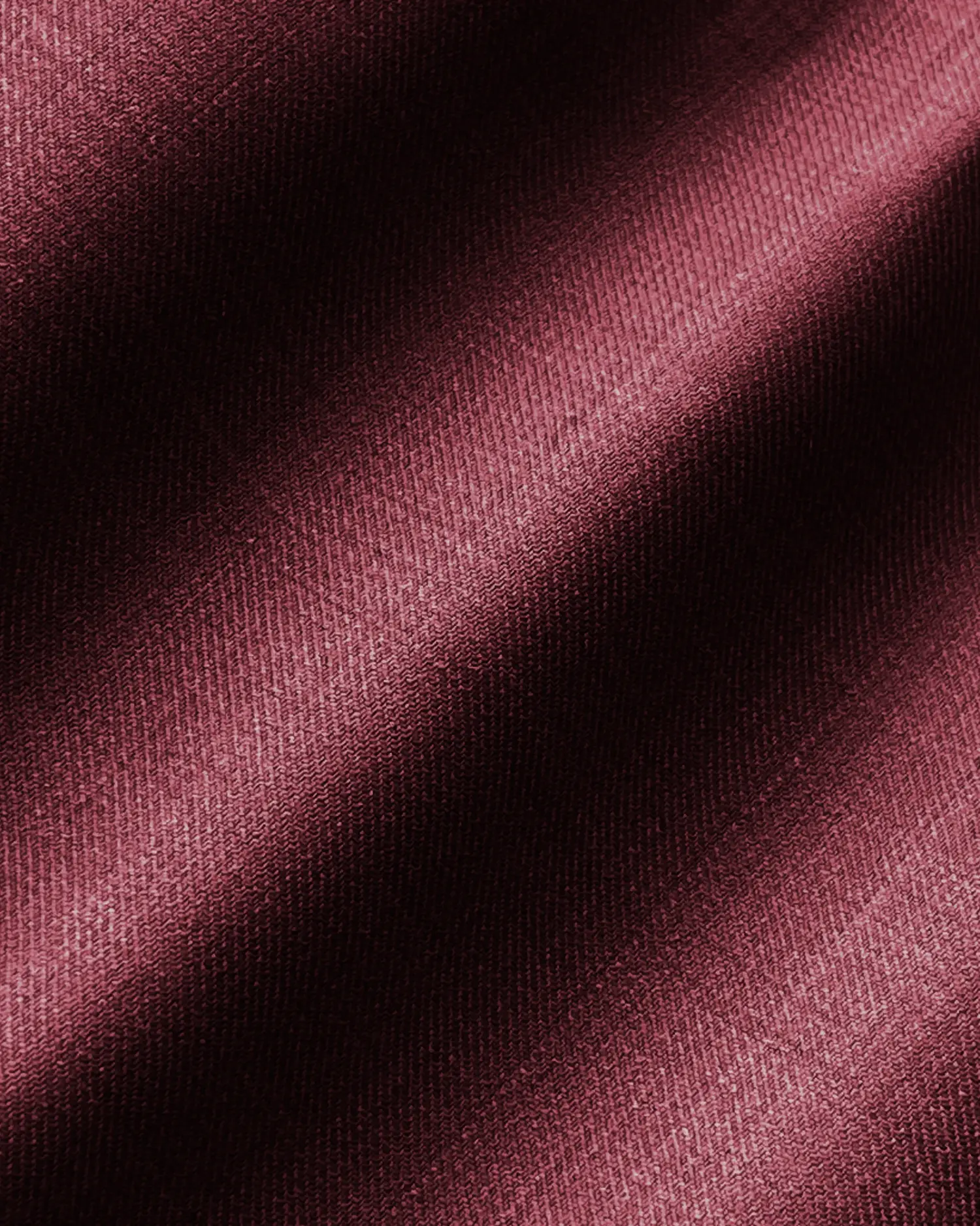 Close-up of maroon textured fabric with diagonal folds, showcasing intricate weave pattern and rich color.