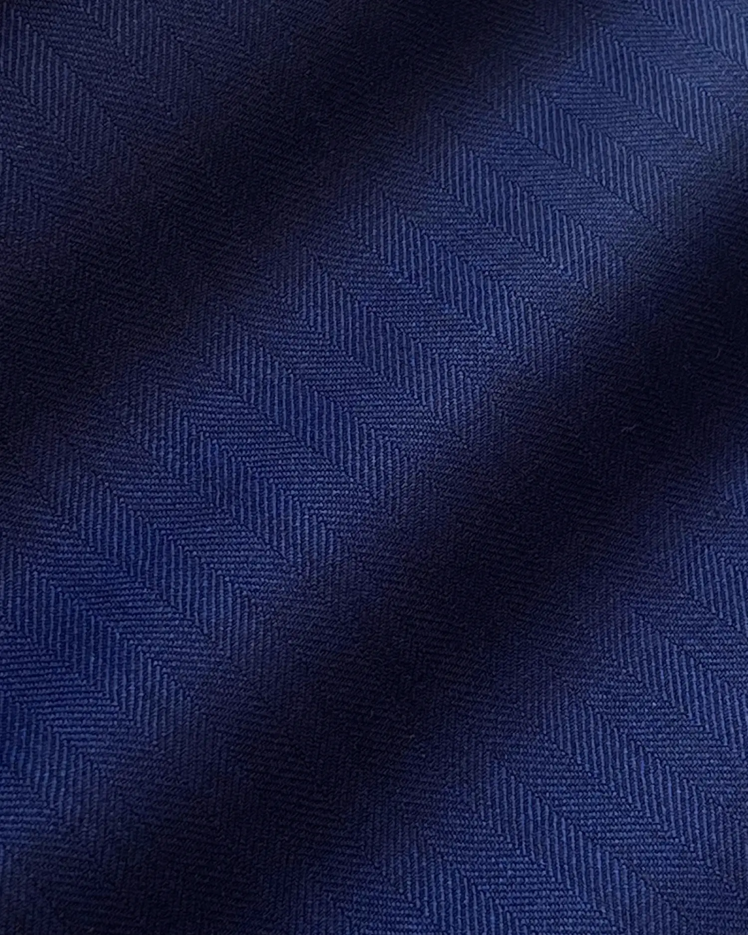 Close-up of a dark blue herringbone fabric texture with soft diagonal shadows, ideal for tailored garments.
