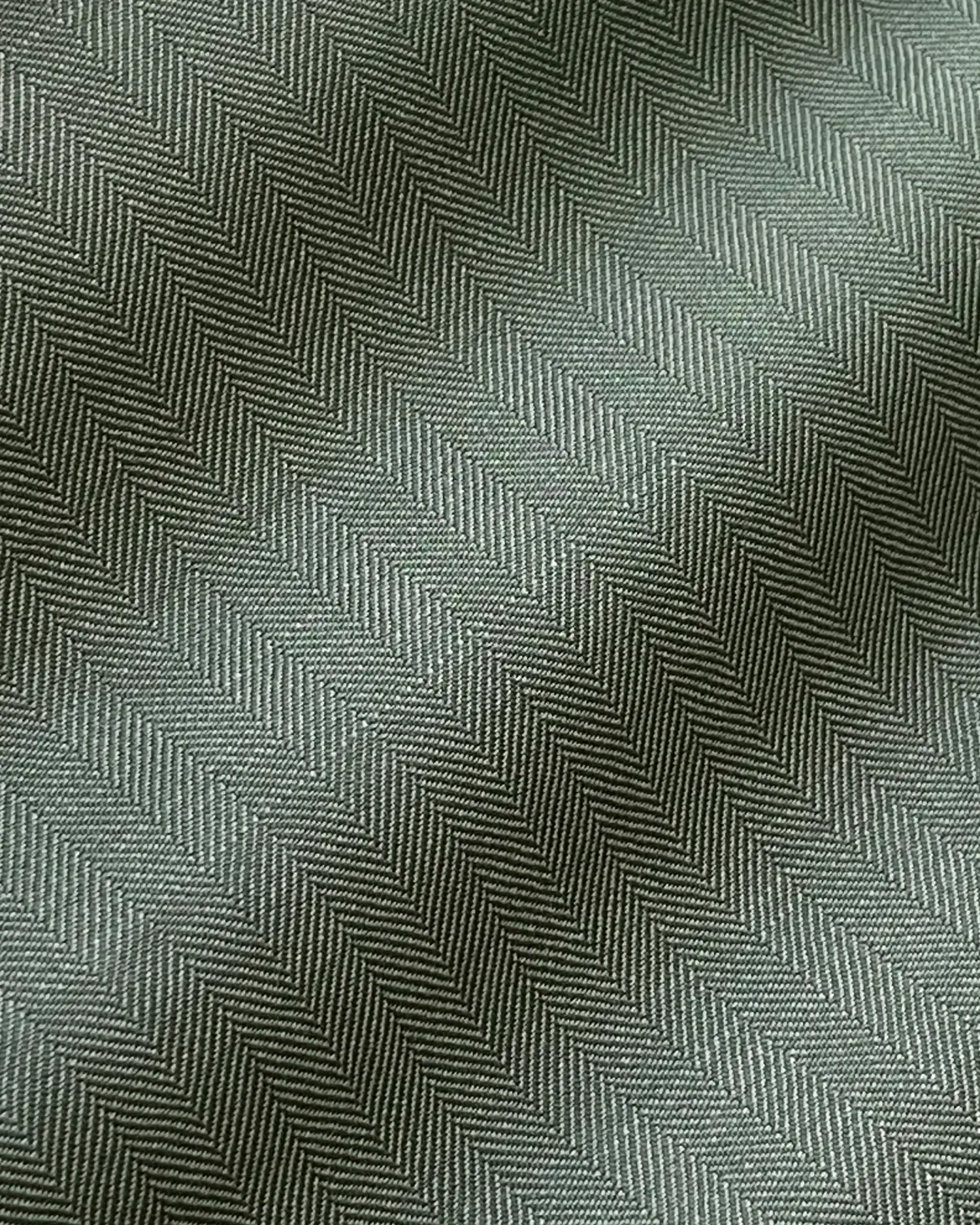 Close-up of green herringbone fabric texture with zigzag pattern, soft light creating subtle shadows.