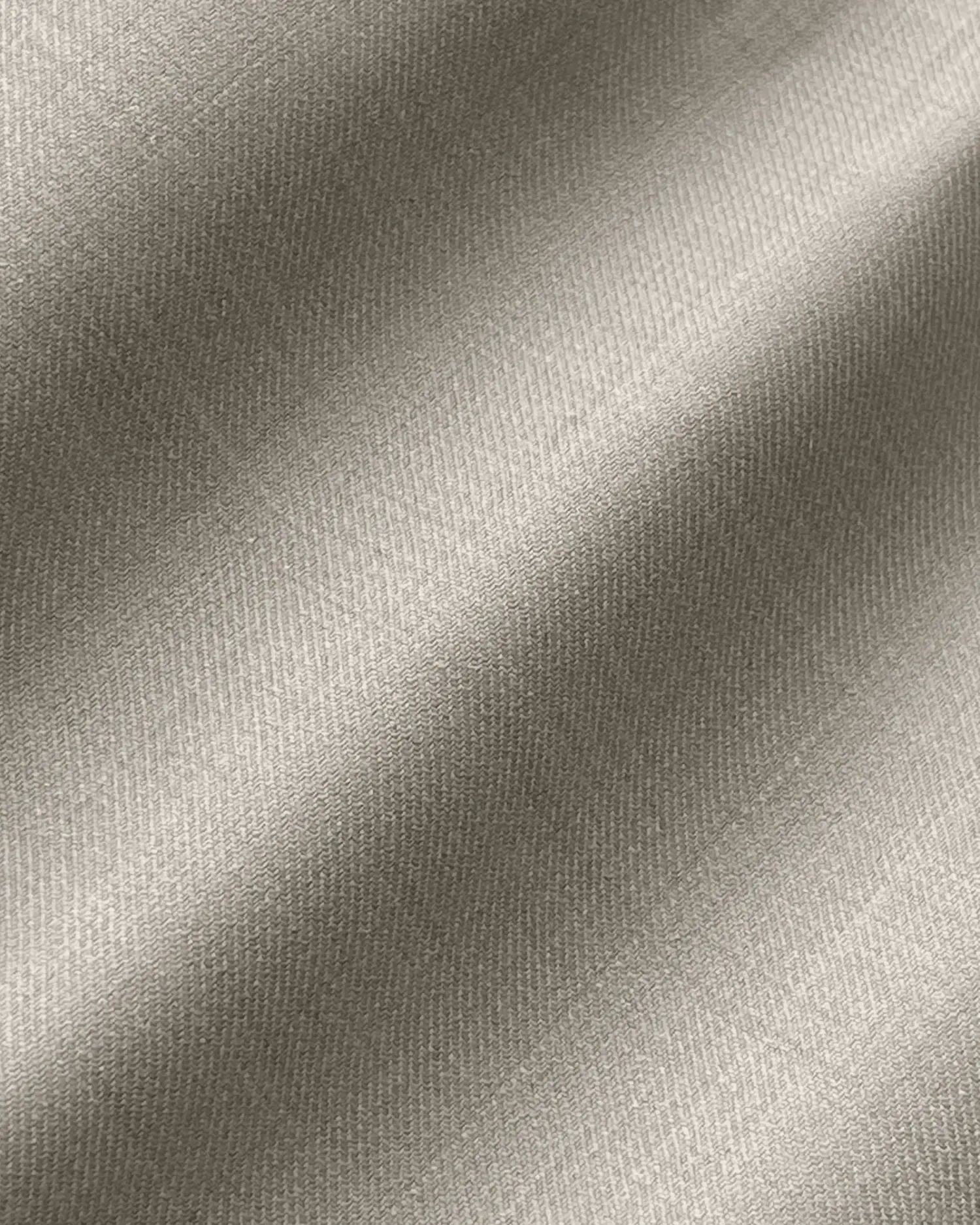 Close-up of a smooth, beige fabric with diagonal weave pattern, showcasing texture and material quality.