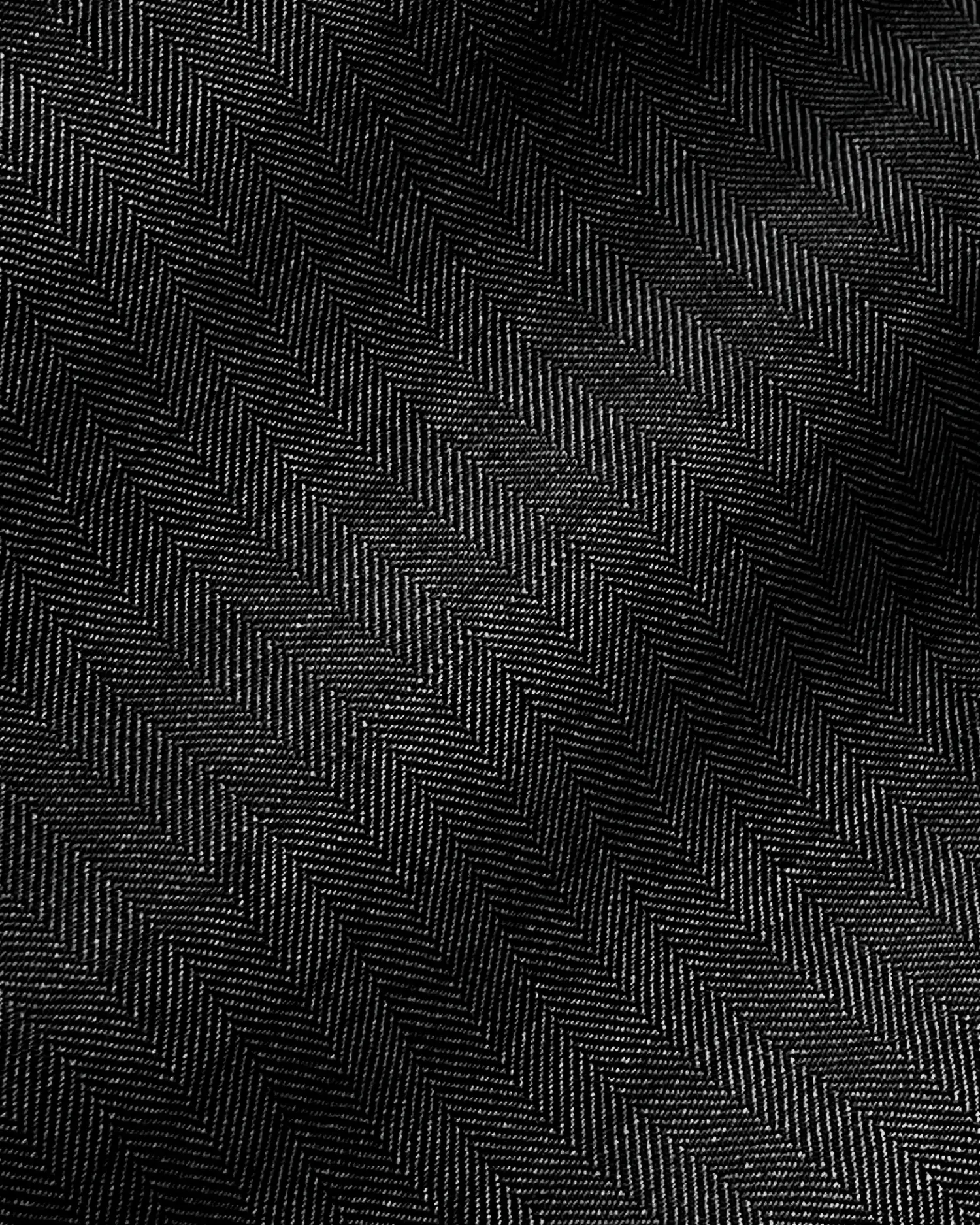 Close-up of black herringbone fabric texture with diagonal zigzag pattern, detailed textile surface.