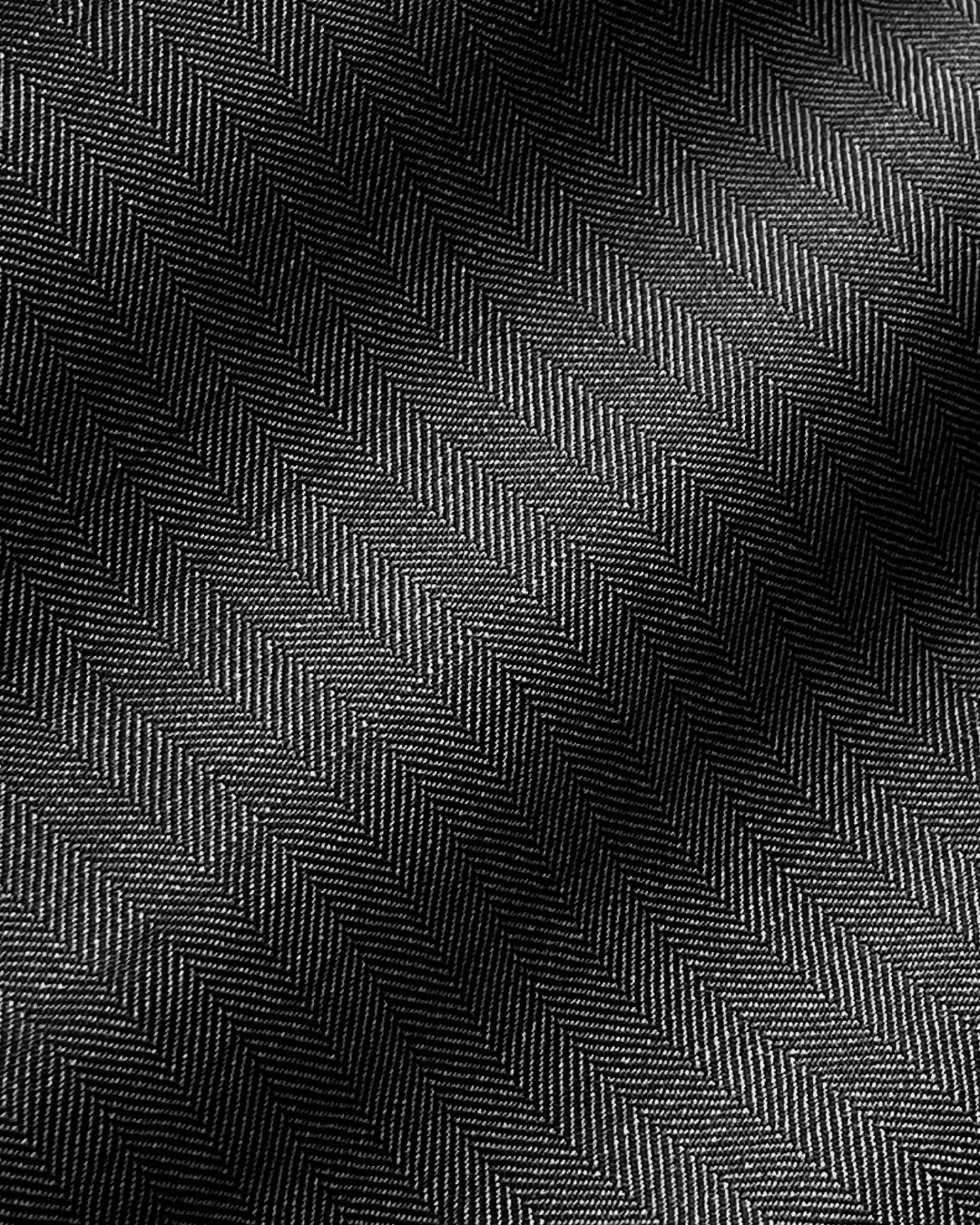 Close-up of black herringbone fabric with detailed zigzag pattern and texture, illuminated by subtle lighting.