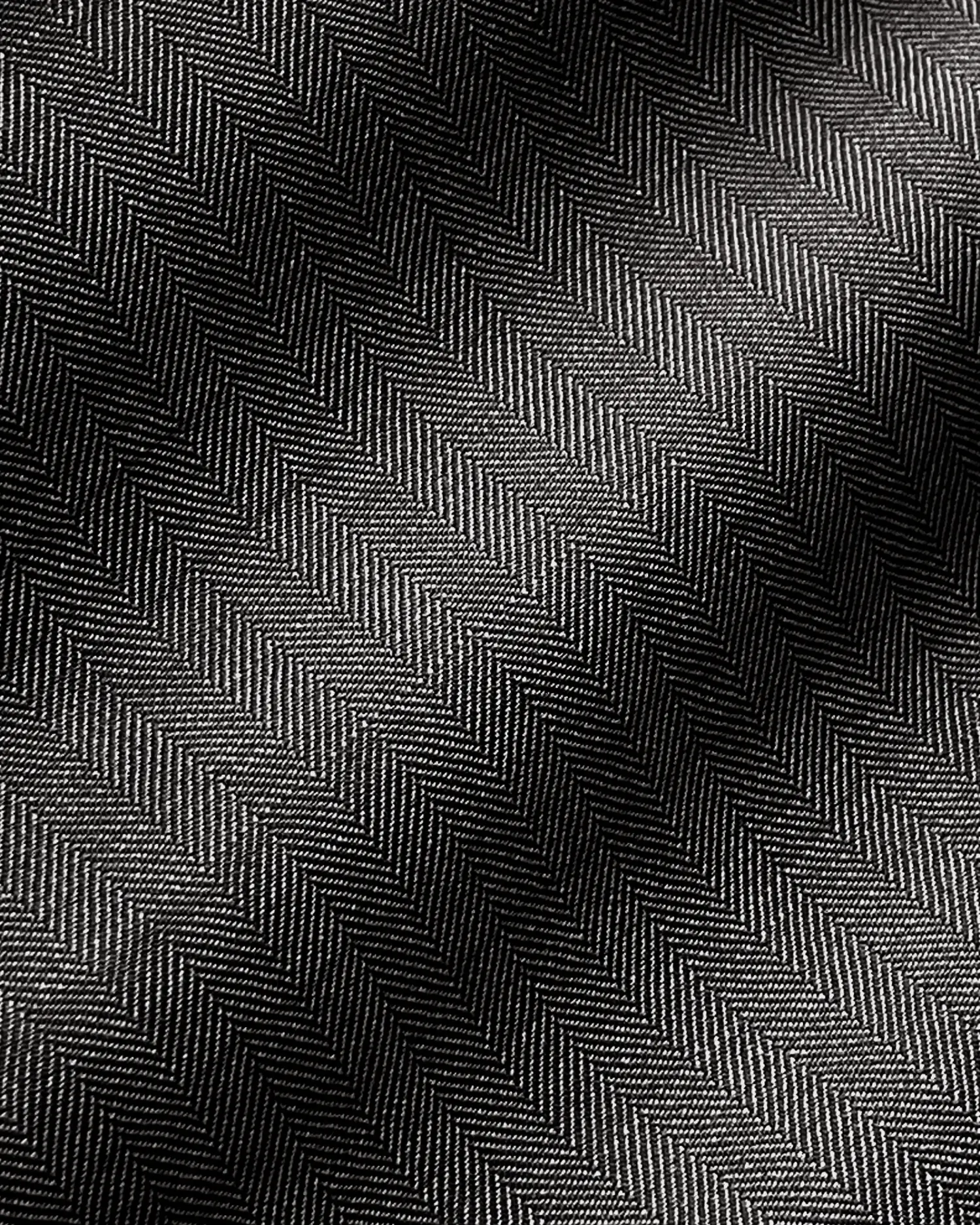 Close-up of dark herringbone patterned fabric with elegant texture and diagonal waves, highlighted by light and shadow.