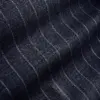 Close-up of dark denim fabric with fine white stitching, creating a subtle wavy pinstripe pattern.