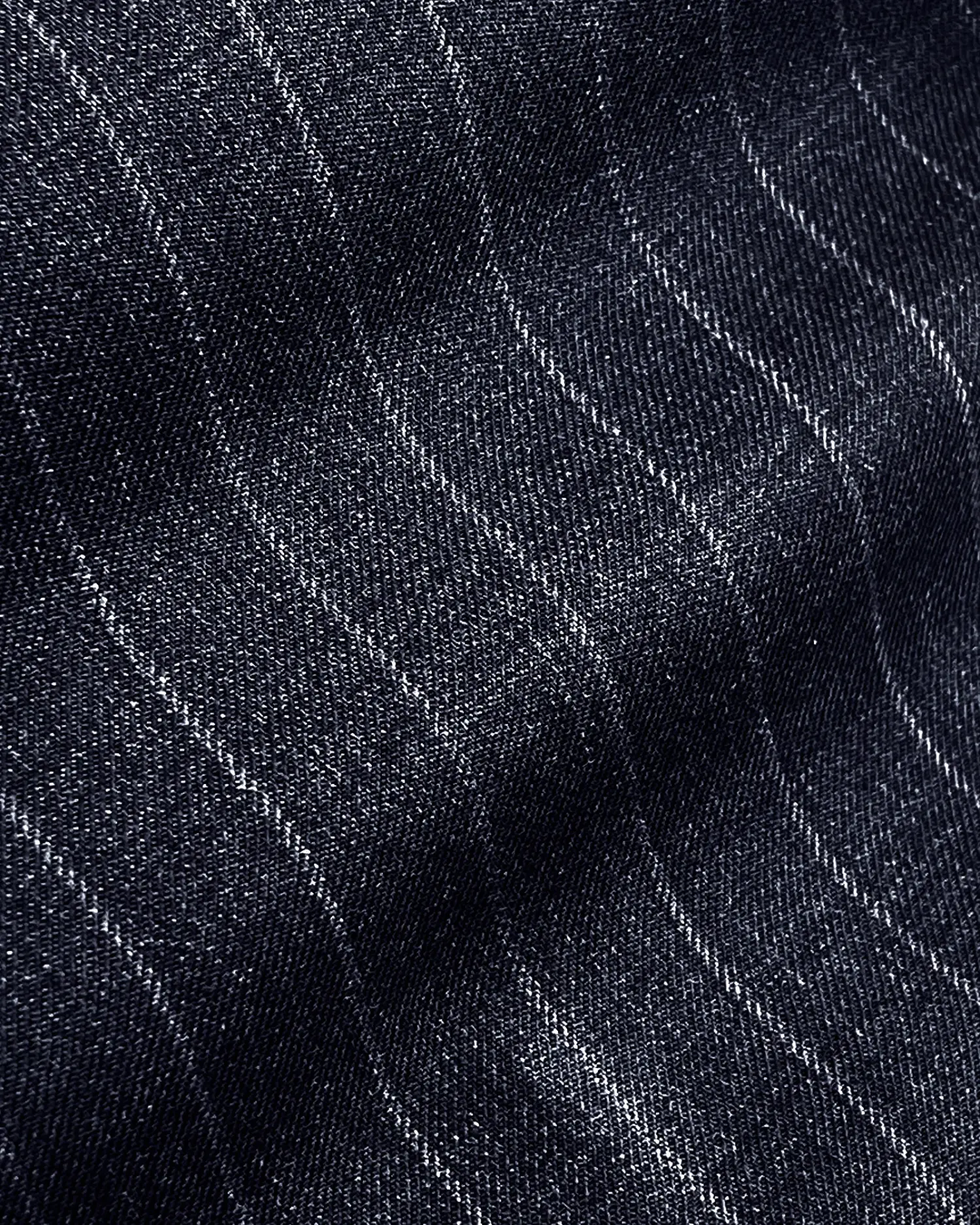 Close-up of dark denim fabric with fine white stitching, creating a subtle wavy pinstripe pattern.