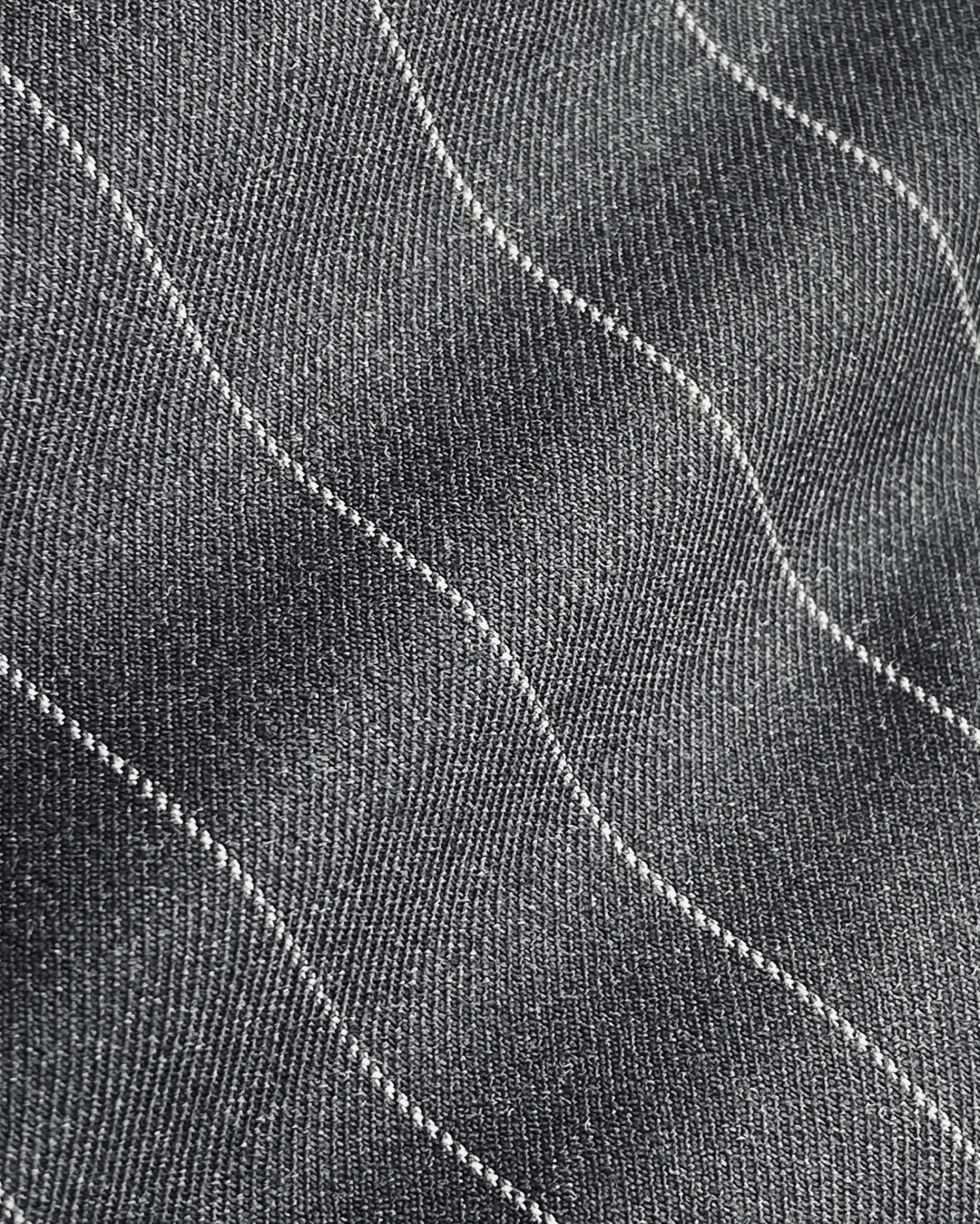 Close-up of black fabric with wavy white stitching, showcasing texture and pattern detail.