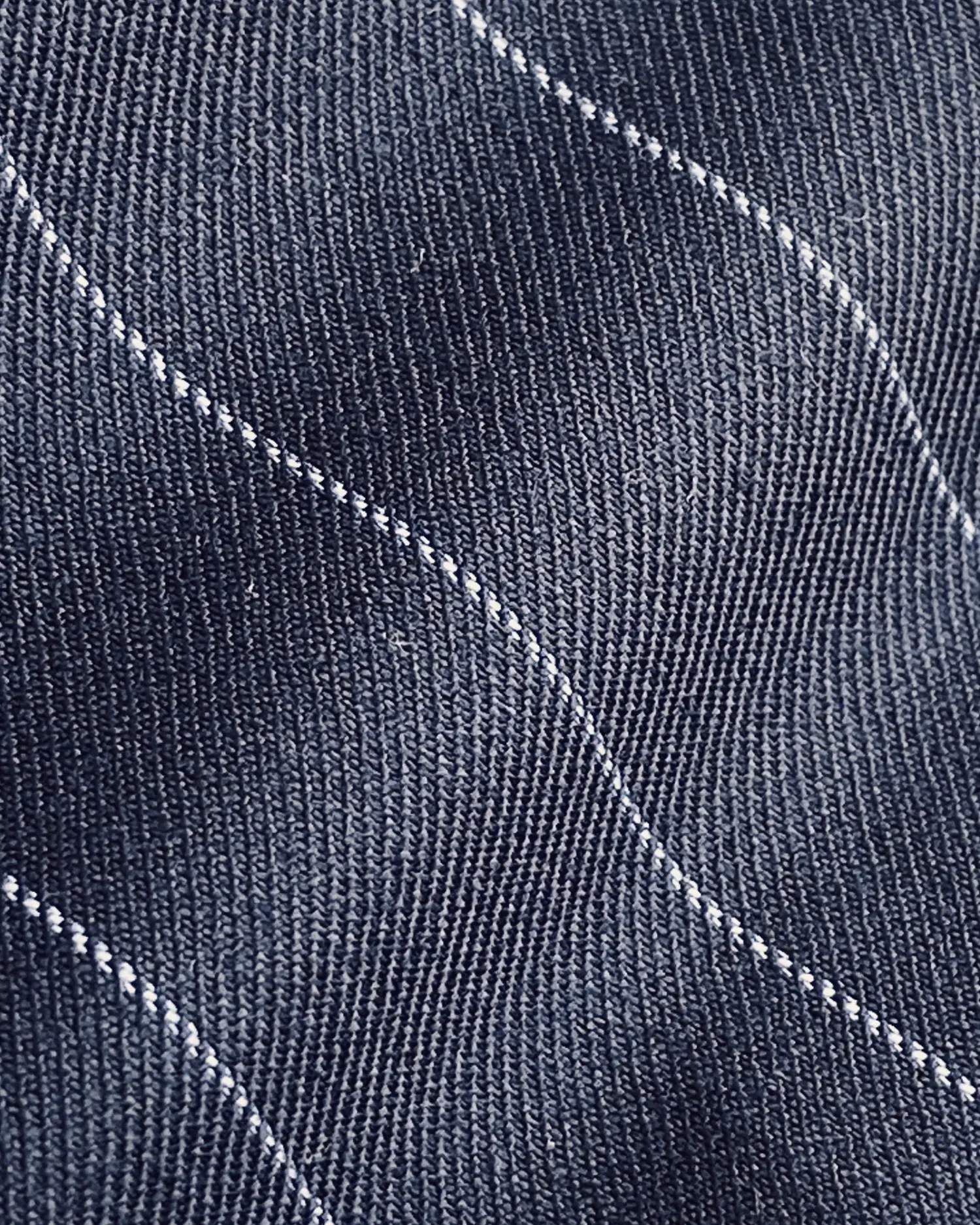 Close-up of dark denim fabric with white stitching creating a wavy pattern.