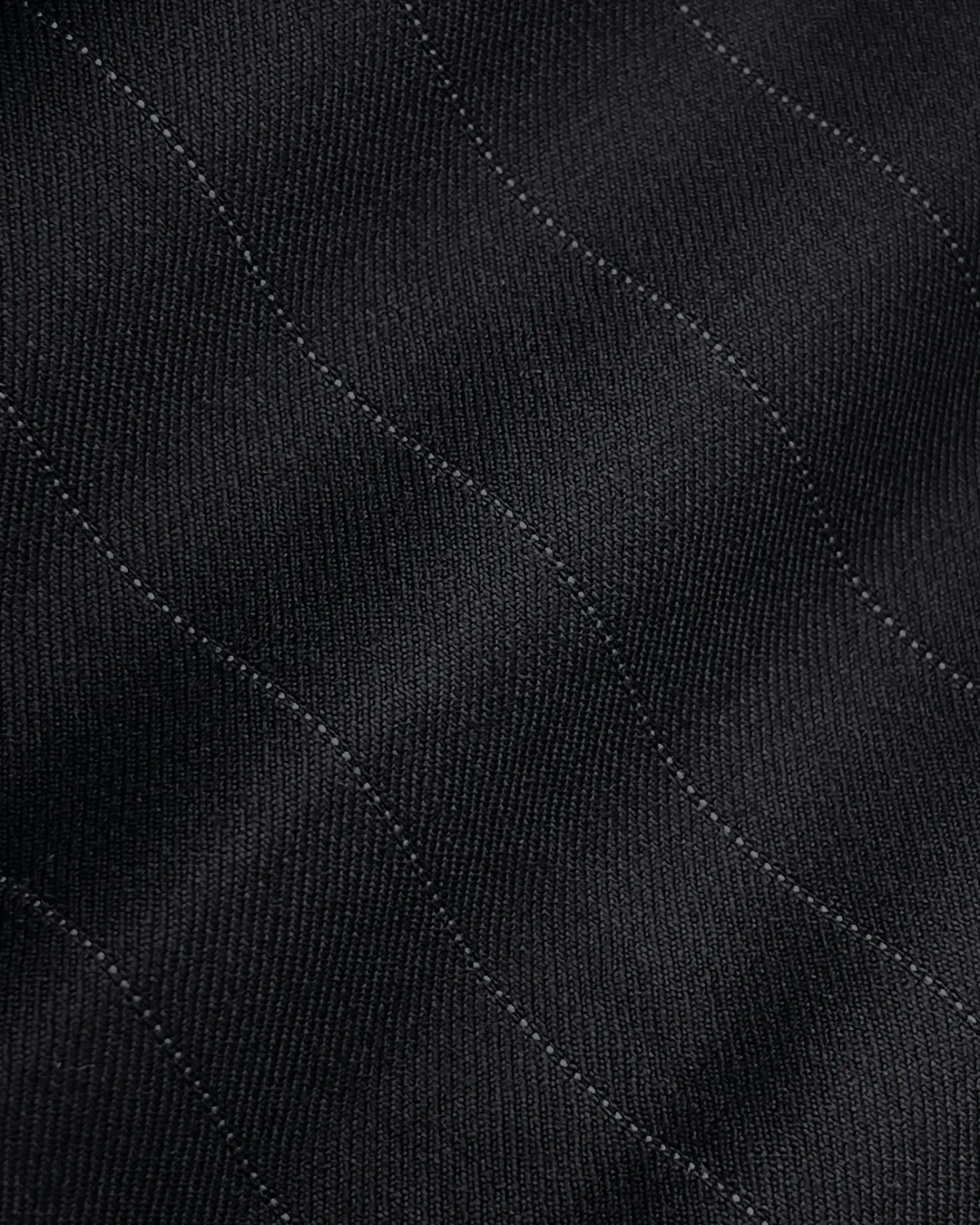 Close-up of black pinstripe fabric with subtle wavy lines, showcasing texture and pattern for clothing design or upholstery.