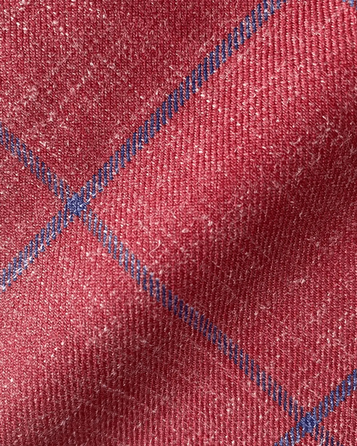 Close-up of red wool fabric with blue check pattern, showcasing texture and detail.