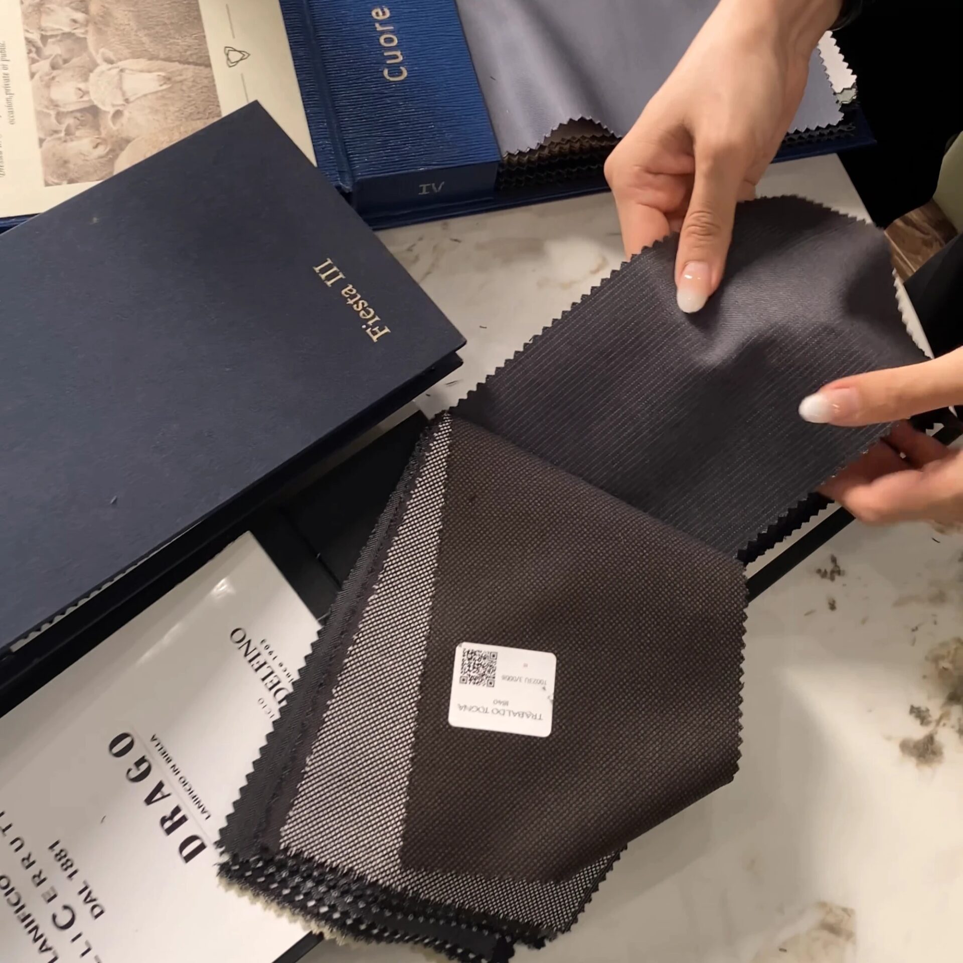 Hands selecting fabric swatches from a selection of textured materials on a table.