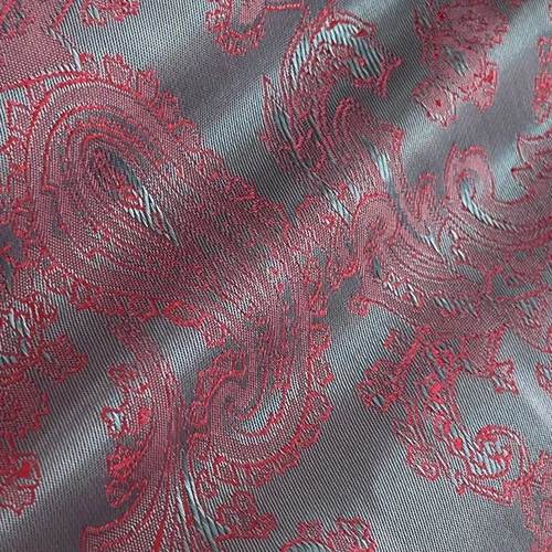 Close-up of intricate red paisley pattern on grey fabric, highlighting texture and design details.