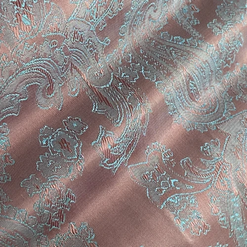 Close-up of ornate light blue paisley pattern on a brown fabric, highlighting intricate textile design.