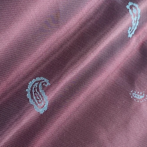 Purple fabric with teal paisley pattern, close-up view showing intricate texture and design.