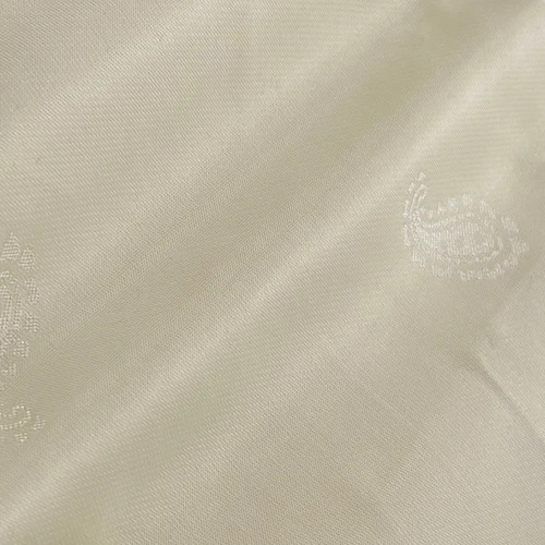 Close-up of ivory silk fabric with subtle embroidered paisley design. Luxurious and elegant textile texture.