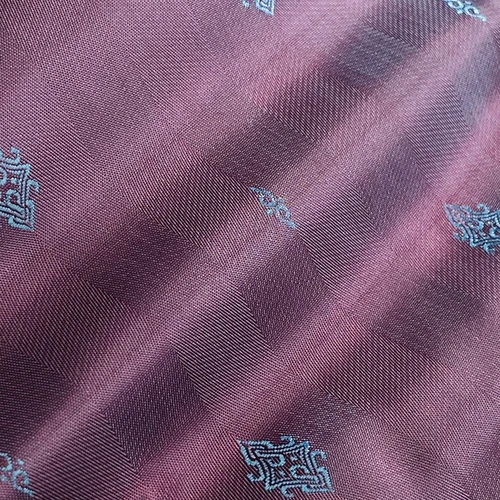 Close-up of purple silk fabric with intricate blue geometric patterns, showcasing detailed texture and design.