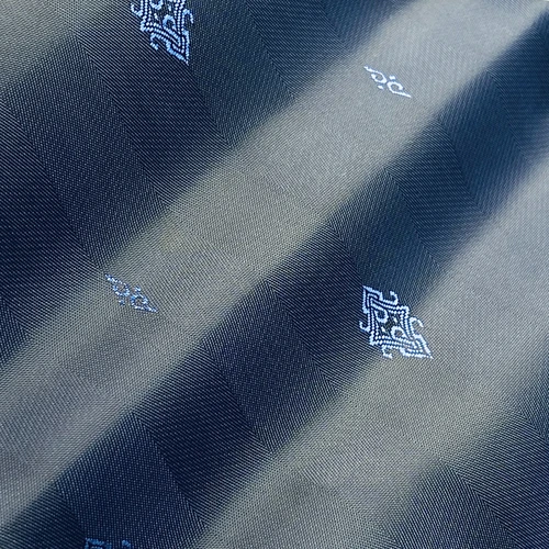 Close-up of elegant silk fabric with intricate geometric patterns and subtle blue hues, showcasing detail and texture.