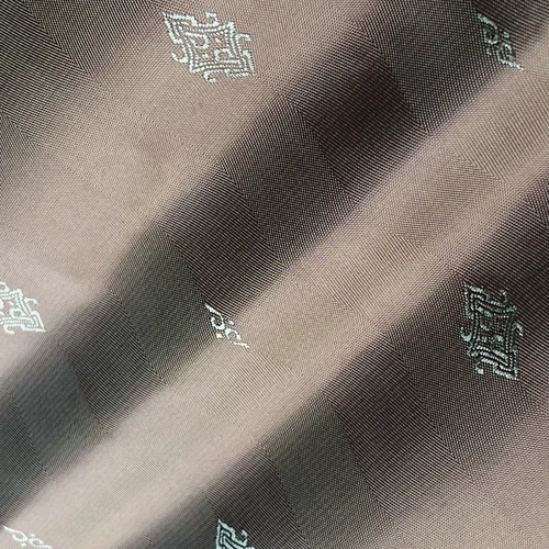 Close-up of detailed beige fabric with intricate silver embroidery, creating a pattern of geometric motifs.