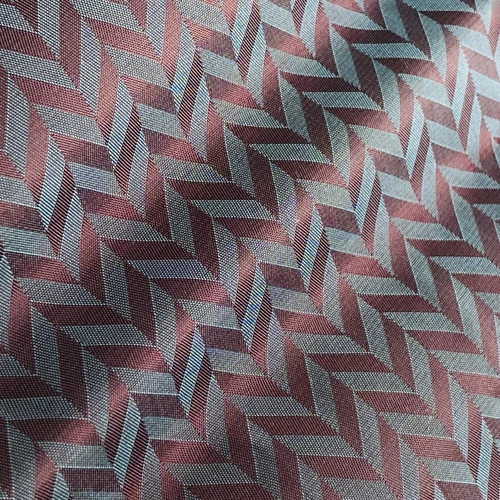 Close-up of fabric with red and gray herringbone pattern, featuring textured diagonal lines for a modern design.