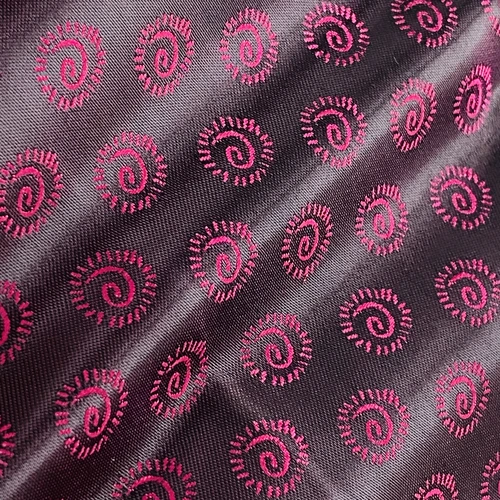 Close-up of fabric with pink spiral patterns on dark background, showcasing intricate textile design and texture.