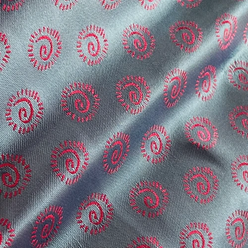 Blue fabric with pink spiral embroidery pattern, creating a vibrant and textured textile design.
