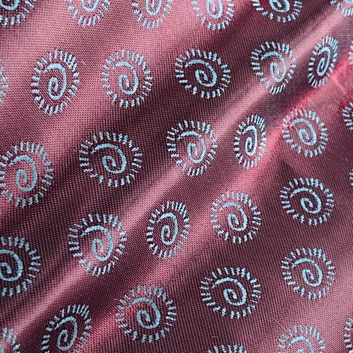 Close-up of maroon fabric with embroidered blue swirl patterns, showcasing detailed textile design.