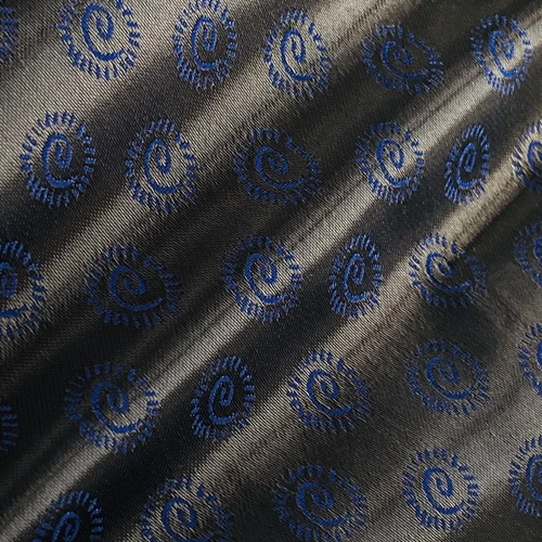 Close-up of blue spiral patterns on dark fabric, showcasing intricate textile design and texture.