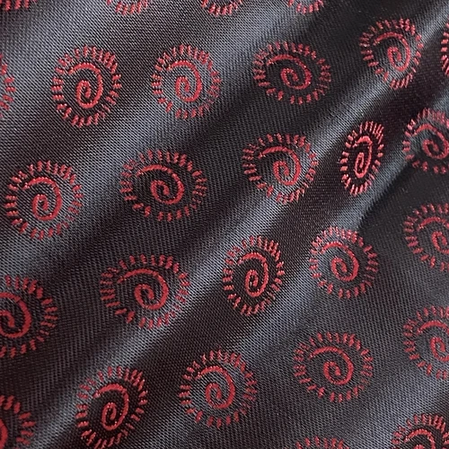Close-up of black fabric with red spiral embroidery patterns creating an elegant, textured design.