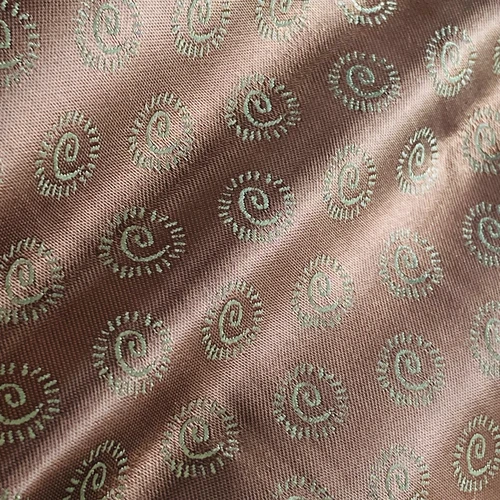 Close-up of intricately embroidered fabric with spiral patterns, featuring light green designs on a brown background.
