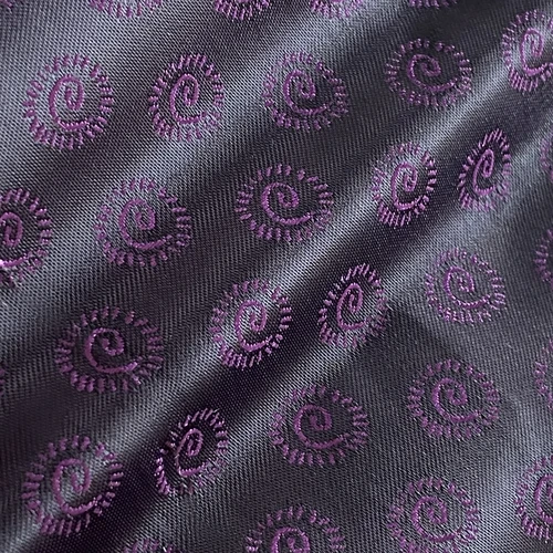 Purple spiral pattern on textured fabric background with diagonal folds, creating an elegant and intricate design.