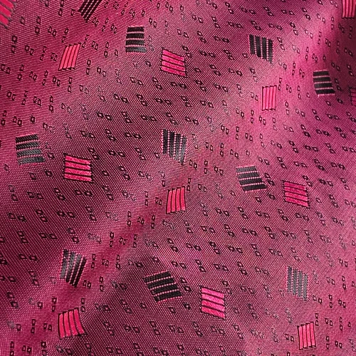 Close-up of pink fabric with geometric patterns, featuring squares and rectangles in black and red.