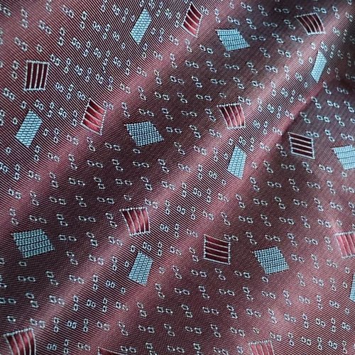 Close-up of burgundy fabric with geometric patterns in red, blue, and white, featuring squares and intricate designs.
