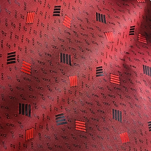 Red fabric with geometric patterns, including squares and stripes, creating a textured and stylish design.