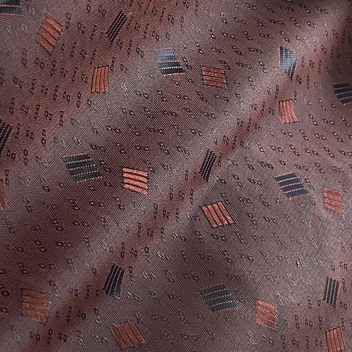 Brown fabric with geometric patterns and red and black designs, featuring textured, diagonal lines.
