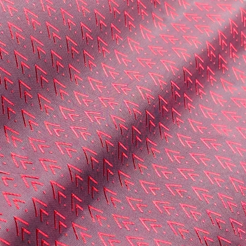 Red-patterned silk fabric with geometric arrow design, close-up texture shot.