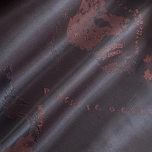 Close-up of textured fabric with a world map design in dark brown hues.