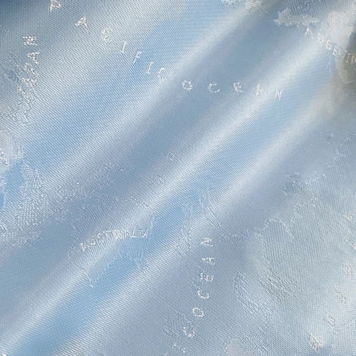 Close-up of light blue silk fabric with embossed world map patterns, highlighting the Pacific Ocean.