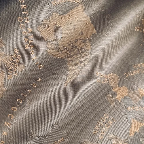 Close-up of fabric with embossed world map design in gold and gray tones, showcasing continents and ocean names.