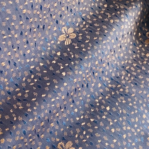 Intricate blue fabric with a dotted pattern and subtle flower motifs, showcasing elegant textile design.
